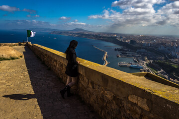 Lonely woman staring at the horizon at Fort Santa Cruz, one of the three forts in the city of Oran, the second largest port city of Algeria above the Gulf of Oran - obrazy, fototapety, plakaty
