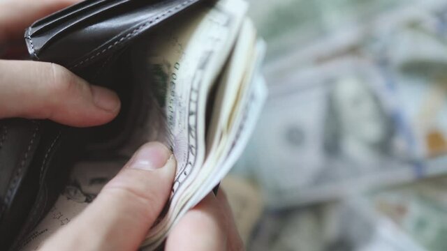 female hand taking out pulling out US dollar bills banknotes cash from black wallet purse.