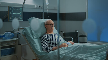 Sick old man staying in hospital ward bed with oximeter and nasal oxygen tube while waiting for...