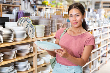 Portrait of focused asian woman buyer choosing dishes at decor store