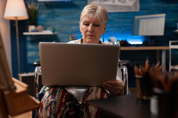 Old artist with handicap looking at laptop in workshop for creativity. Senior disabled adult...