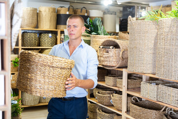 European man in shirt choosing wicker basket in housewares store.