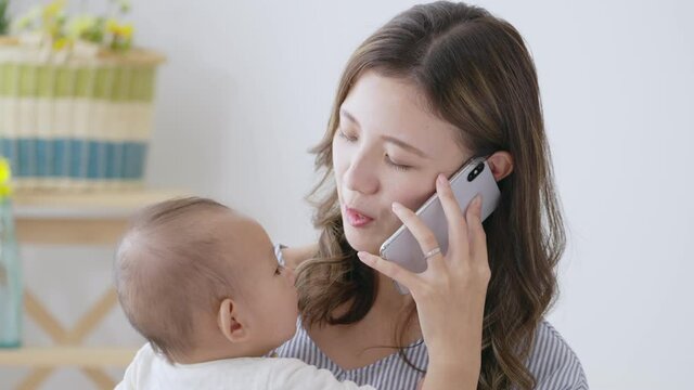 赤ちゃんを抱っこしてスマホで電話するママ（育児・子育て・家族・ファミリー）