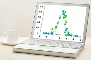 graph of data following Gaussian distribution (bell curve) on a laptop with a cup of coffee,...
