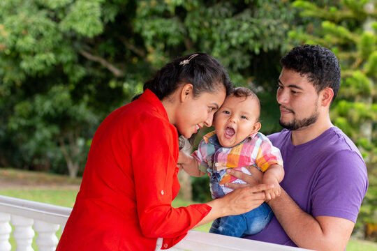 Smiling parents playing with their baby in a beautiful park full of nature. latin family concept.