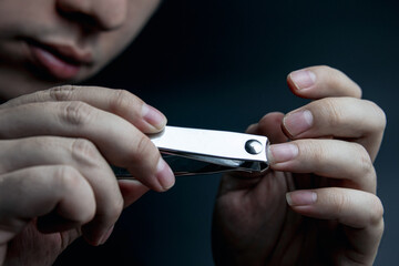 Nail clipper in hand. A young man cuts his nails on a black background. concept of health care