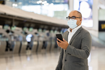 Young businessman wearing mask to protect flu coronavirus Covid-19.He drag luggage walking in terminal. Tourist in airport terminal using smartphone check in at counter.