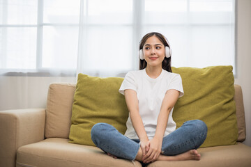 Obraz premium Relaxing time on sofa. Beautiful young asian woman sitting on sofa she choose music from smartphone take a rest and listening song with headphone. Lifestyle in living room at house in the morning.