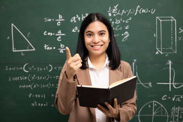 Young asian teacher woman teaching holding book and video conference with student looking camera. Female teacher training the mathematics in classroom blackboard from online course.