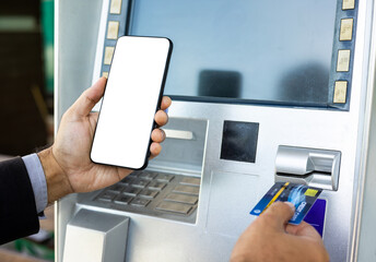 Young businessman standing front of atm machine using smartphone withdraw the money without atm credit card. He ut the pin code into smartphone and take the money.