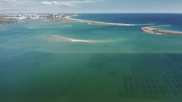 Panoramic view of picturesque beach filling with kitesurfers in Alvor, Portugal, Europe. Drone shot of sportsmen gliding in the Atlantic ocean on kiteboards. People kiteboarding on beach, 4k footage