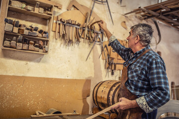 Older artisan picks necessary parts for making wooden products in a rustic workshop