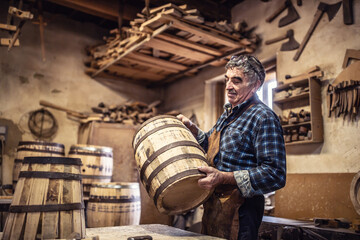 Fototapeta na wymiar Craftsman puts finished wooden barrel on a table in his rustic workshop