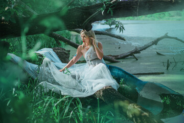 A beautiful girl in a transparent white cloth sits on a branch in a swamp. A mermaid with a diadem...
