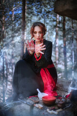 A witch in a black long dress of Slavic style is holding a magic rite in the mountains.