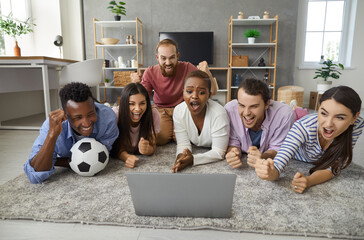 Group of multiracial friends lying on the floor in front of laptop emotionally watching a football match. Women and men gathered on the weekend to watch a football match. Concept of human emotions.