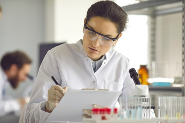 Portrait of serious scientist in white lab coat collecting data in medical research laboratory....