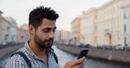 Young indian tourist man smiling using smartphone at city