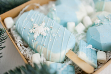 An open cardboard box with Christmas cakes. Different confectionery cakes of blue color. Chocolate, spruce branches, decoration in the form of snowflakes.