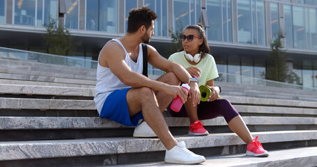 Fit diverse couple taking rest after workout outdoors, sitting on urban stairs - Powered by Adobe
