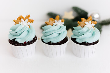 Chocolate cupcakes with blue cream on a white background. Decor of spruce branches, decoration in the form of sugar snowflakes. Christmas and New Year.