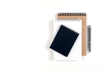 Three blank notepads on a spiral stacked in a stack on a white background. Notebooks with white, black and recycled sheets and pen. Education, office.