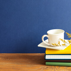 Stack of notebooks and coffee cup on wooden desk. blue wall background