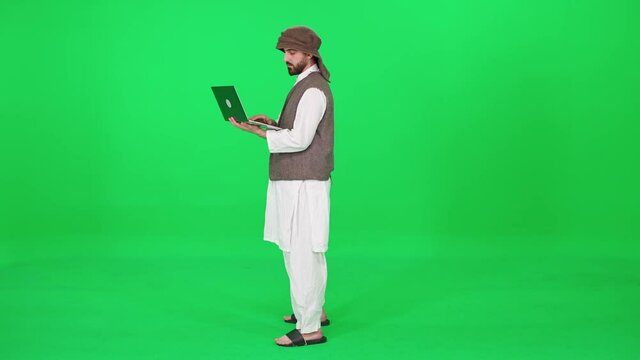 Freelancer, man of Arab appearance in traditional clothes uses a laptop to surf the internet while stands against the background of a chromakey.