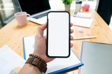 Cropped shot of man hand holding blank screen smartphone while sitting at office desk.