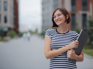 young pretty asian woman walking with laptop in modern city street on remote IT work, summer style casual smiling