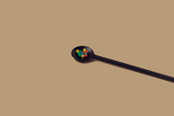 Single black teaspoon with colorful sugar ball sprinkles on a yellow background with sharp shadows...