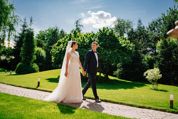 the bride and groom walk holding hands along the path in the park.