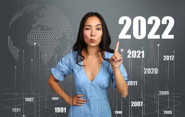 Asian woman pointing at figure 2022 on dark background