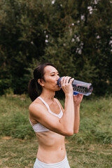 Asian woman drinking water outside after working out