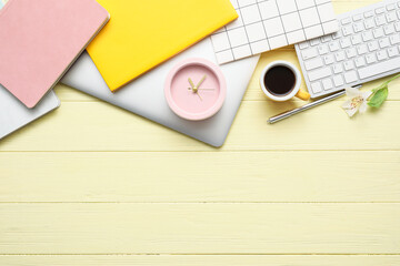 Alarm clock with office supplies, cup of coffee and laptop on color wooden background