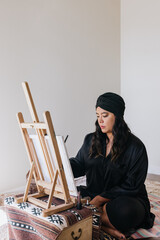 Filipino woman painting on easel while sitting on floor