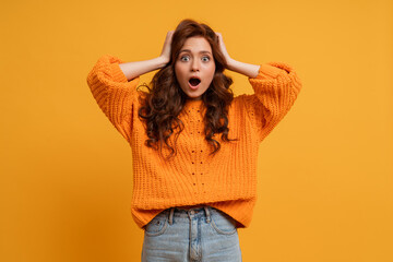 Excited young girl in  orange  sweater  posing in studio  with  wavy  hair isolated on yellow...