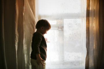 Obraz premium Cute kid toddler in warm sweater near the window in cozy interior, bedroom in warm colors