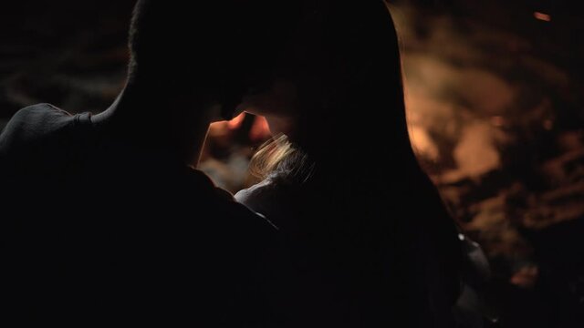 close-up portrait Caucasian couple man and woman sit in the evening on the beach by the fire and kiss.