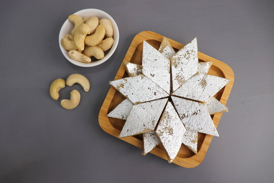 Kaju Katli is a traditional Indian Diamond shaped sweet or Mithai made using cashew paste, sugar, and mava or Khoya. served in a wooden plate over dark background. cashew barfi. Copy space
