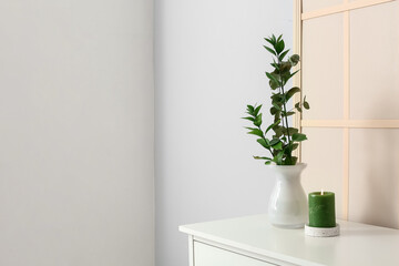 Chest of drawers with candle and eucalyptus branches near light wall
