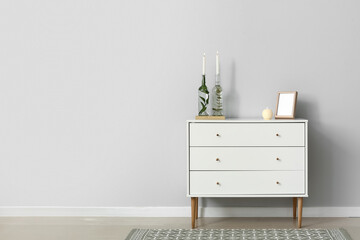 Modern chest of drawers with candles and frame near light wall