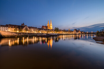Fototapeta na wymiar Regensburg während der blauen Stunde im Zwielicht mit Donau beleuchteter Promenade Dom und steinerne Brücke, Deutschland