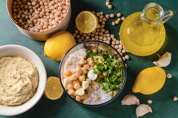 Blender with chickpeas and ingredients for hummus on color background