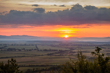 Dawn in the mountains. The sun rises from behind the mountains. Beautiful green hills and green valley. Little sleeping town. A colorful sky, red clouds. Mountains in the fog. Carpathian, Ukraine,