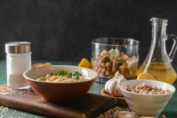 Bowl with tasty hummus and ingredients on dark background