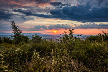 Dawn in the mountains. The sun rises from behind the mountains. Beautiful green hills and green valley. Little sleeping town. A colorful sky, red clouds. Mountains in the fog. Carpathian, Ukraine,