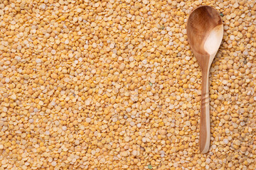 A wooden spoon lies on dry yellow peas. Top view