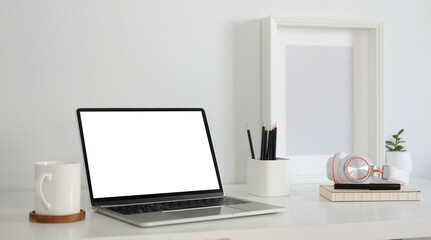 Mock up laptop computer, coffee cup, pencil holder and picture frame on white table.