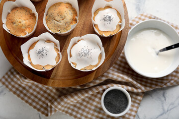 Wooden board with delicious glazed poppy seed muffins on table